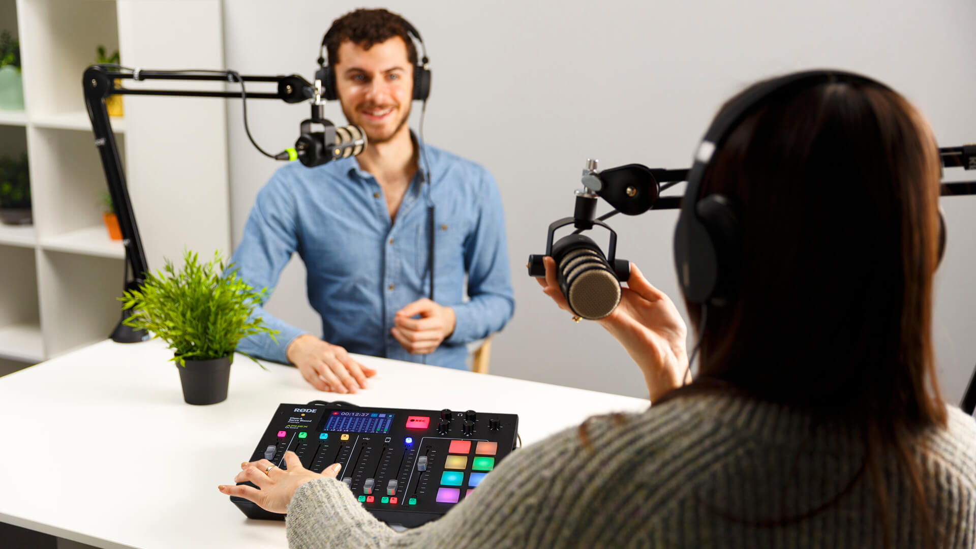 Two podcasters wearing headphones recording with RØDECaster Pro, PodMics and PSA1 s