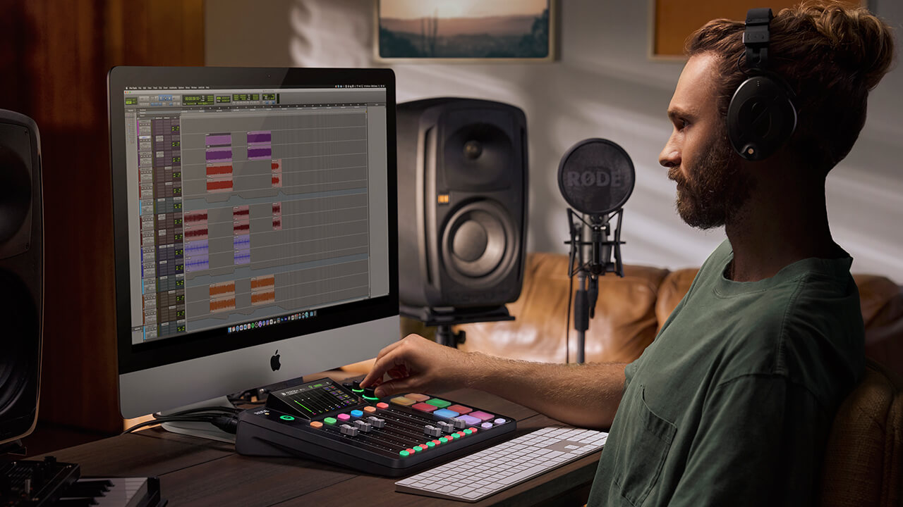 Man with hand over RØDECaster Pro II in front of computer screen showing Pro Tools